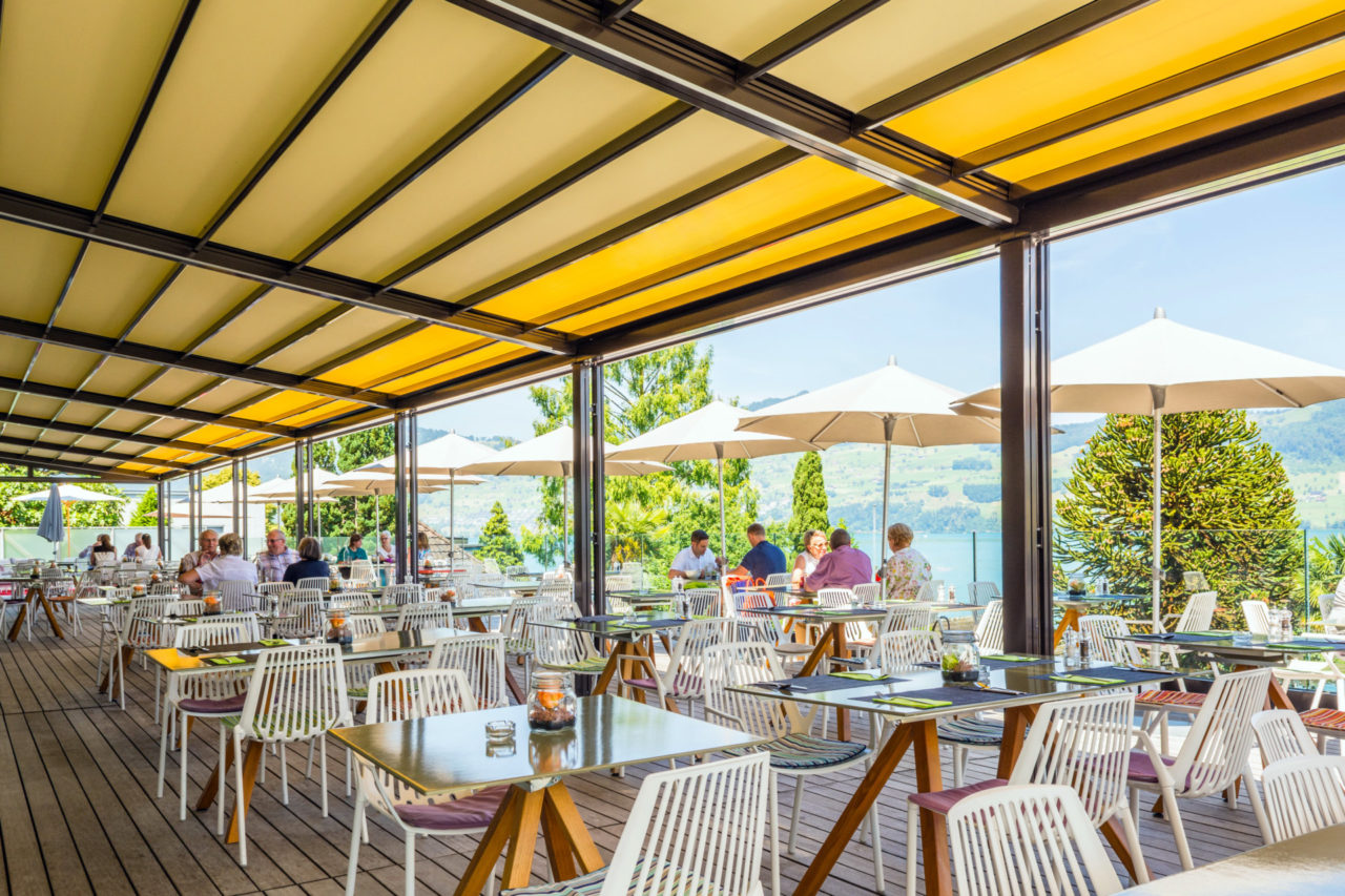 Klaiber Markise, Gastromarkise RIVERA P 5000, optimaler Wetterschutz Die Gastro- Markise, RIVERA P5000, ist die Nummer 1 auf Ihrer privaten Terrasse oder für große Flächen in der Außengastronomie. Sie ist entwickelt für besondere Größen. Manchmal darf es eben etwas mehr sein. Besonders große Terrassen bieten viel Komfort, deshalb sind die Anforderungen an den Schutz vor Sonne, Wind und Regen auch besonders hoch. Das multifunktionelle Terrassendach RIVERA P5000 bietet im Standard bis zu 105 m² zuverlässigen Sonnenschutz und Regenschutz. Mit der neuen RIVERA P5000 kreieren Sie auf jeder Terrasse großzügigen Freiraum im eleganten Design. Die integrierte Faltmarkise spendet bei Sonnenschein kühlen Schatten und schützt vor schädlicher UV- Strahlung. Wenn es regnet, leitet das straff gespannte und wasserdichte RESISTANT- Polyestergewebe das Wasser kontrolliert zum Ablaufsystem im Frontbereich. Erweitern Sie den Open-Air- Genuss mit komfortablen Optionen. Die stromsparende LED- Beleuchtung zaubert nachts ein stimmungsvolles Ambiente auf Ihre Terrasse. Mit den variablen Schiebeverglasungen profitieren Sie von zusätzlichem Schutz gegen Wind und Wetter und verlängern dadurch Ihre Freiluft-Saison - Panoramaausblick inklusive. Auf Wunsch sorgt die harmonisch integrierte, dimmbare LED- Beleuchtung für Terrassengenuß bis tief in die Nacht hinein. Infrarotstrahler sorgen für wohlige Wärme von der ersten Sekunde an. Die Bedienung per Funk ist ebenso möglich. Exklusiver kann eine Terrasse nicht vor zu viel Sonne, Wind und Regen geschützt werden! Facts & Figures Großflächiges, maßgefertigtes Terrassendach Elegante Sonnen- und Regenschutzlösung Flexibel einsetzbar für Privat und Gastronomie Regendichte Faltmarkise mit robustem, schmutzabweisendem Polyestergewebe, Brandschutzklasse B1 Integrierter Wasserablauf Dachneigung von 8° bis 25° Korrosionsbeständige Aluminiumkonstuktion Serienmäßig mit Elektroantrieb Komfortabel erweiterbar durch: Integrierte, dimmbare LED- Beleuchtung Schiebbare Seiten- und Frontverglasung Aluminium Systemboden,Klaiber Markise, Gastro-Markise, RIVERA P 5000, Terrassenüberdachung, Terrassen- Pavillon, MELANO TP7000, Wintergarten, Kaltwintergarten, Sonnenschutz, Wetterschutz, Regen- Markise, Wasserdichte Markise, multifunktionelles Terrassendach, Glasschiebewand, Schiebeverglasung